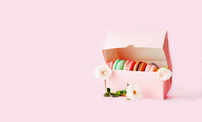 Gift box with colored macaroons on pink background with white roses. Bold hues for seasonal projects and basis designs. 