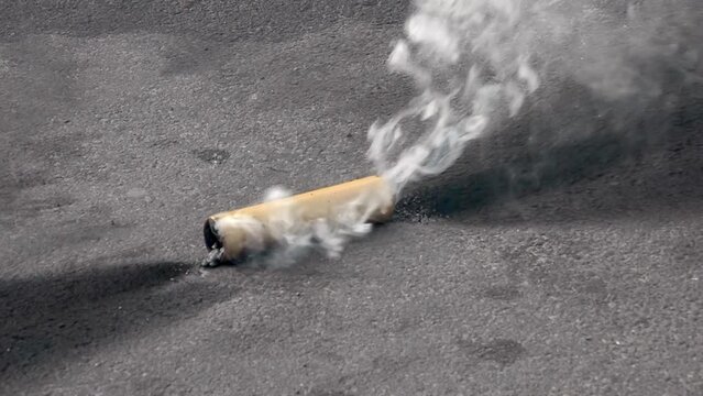 A smoking smoke bomb on the street during a protest. White thick smoke close up. Riots and hooliganism on the streets of the city. Close-up of a burning flare.