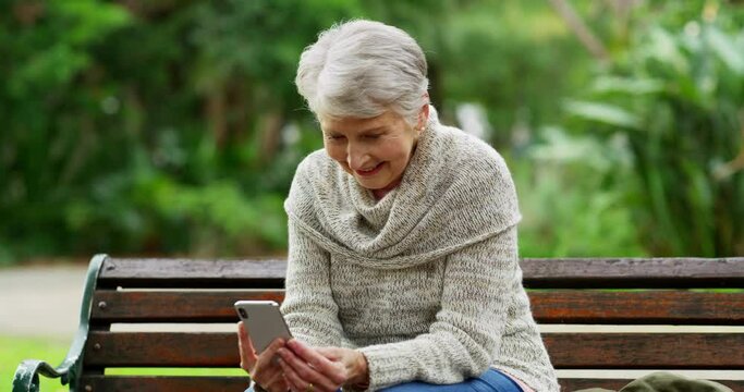 Selfie, relaxed and senior woman holding a phone while sitting on a park bench and enjoying fresh air on a sunny day. Happy elderly lady doing video call and smiling while sitting outdoors in nature