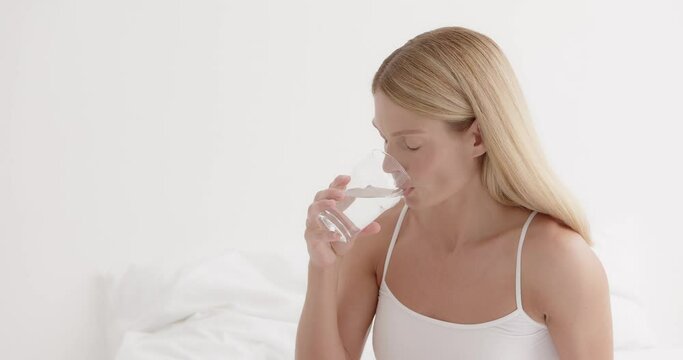 Beautiful lady holding glass of mineral water, hydrating her body in the morning