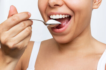 Cropped shot of a young woman bringing a spoonful of sugar to her mouth isolated on a white...