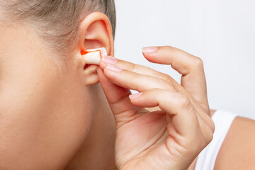 Close up of a young woman putting polyurethane earplugs in her ears with her hand isolated on a...