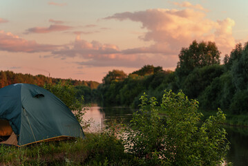 A tent on the river bank against the background of an evening summer sunset.