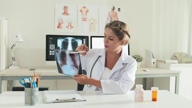 Female doctor showing chest x ray scan and explaining it on camera while giving online consultation or filming medical vlog in clinic