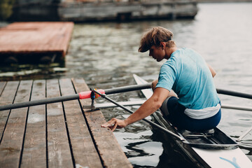 Sportsman single scull man rower prepare to training competition with boat on pier river - obrazy, fototapety, plakaty