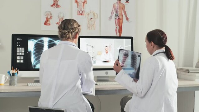 Female doctors sitting at desk in clinic and discussing chest x ray scan with colleague via video call on computer