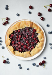 Fresh cherry and blueberry galette with coconut on white plate, top view, white background. Homemade rustic dessert - american pie or tart or cake or french galette