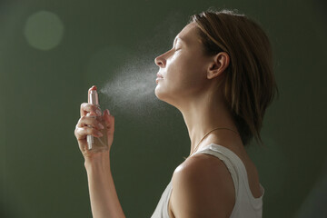 Woman spraying facial mist on her face, summertime skincare concept	