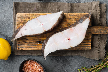 Raw fresh halibut fish steak, with ingredients and rosemary herbs, on gray stone table background,...
