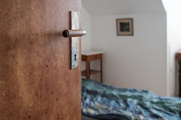Open wooden door, against the background of a bed and a room with white walls, with natural light from the window.