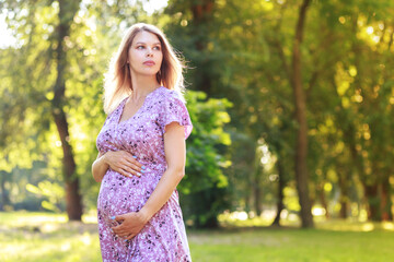 Fototapeta premium Portrait of a pregnant woman walking towards camera looking at side in a park