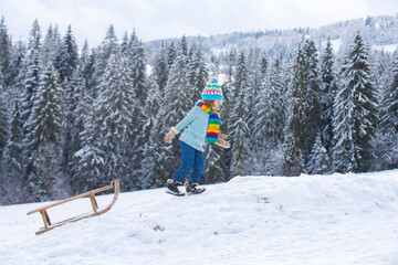 Boy kid sliding with sledge in the winter snow. Christmas kids holidays and Happy New Year. Snow covered trees in the mountains on winter landscape.