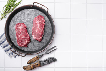 Top blade steak of marbled beef with pepper, on white ceramic squared tile table background, top...
