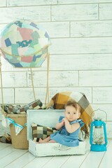 A small newborn baby girl in a blue dress is sitting in a suitcase. The concept of childhood and motherhood, traveling with children