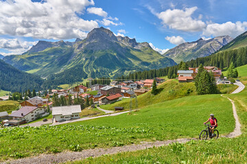 active senior woman, riding her electric mountain bike above famous village of Lech in the Arlberg...