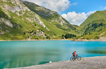 active senior woman, riding her electric mountain bike at Spuller Lake in the Arlberg area near the famous village of Lech, Tirol, Austrian Alps - obrazy, fototapety, plakaty