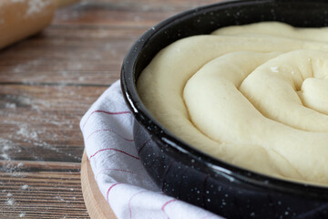 Unbaked pie dough in a baking pan on a wooden table with wheat flour and a rolling pin in the background. A closeup. Traditional homemade Macedonian pastry food, Balkanian cuisine.
