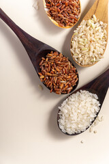 Raw and uncooked rice assortment in wooden spoon on white background. Place for text. Top view.