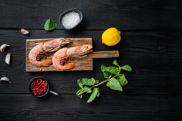Jumbo shrimps on wooden board with herbs on  black wooden background, flat lay with copy space
