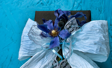Black gift with blue ribbons and clematis flowers in the middle with dark artificial berries