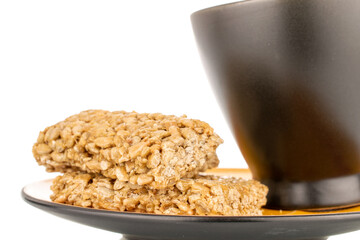 Several sweet roasted sweets from sunflower seeds and honey on a black saucer with a cup, macro, isolated on a white background.