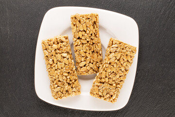 Three sweet candies Grillage from sunflower seeds and honey with a white ceramic saucer on a slate stone, macro, top view.