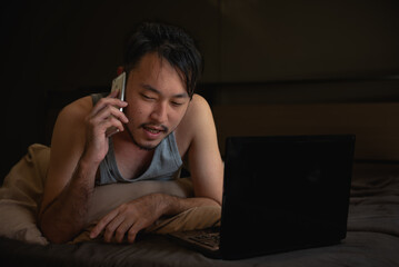 Young Asian man using laptop computer on the bed at night.