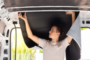 Young man working placing and sticking the rubber isolation in the camper van convertion. As a...