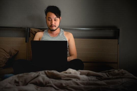 Young Asian Man Using Laptop Computer On The Bed At Night.