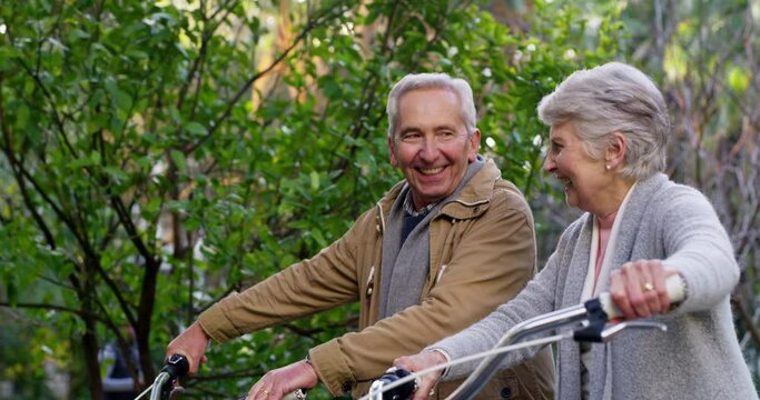 Happy, fun and mature couple talking while walking in a park together, happy and excited to go on a bike ride outdoors. Active seniors enjoying healthy activities while bonding and being cheerful