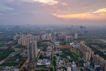 drone aerial shot showing busy traffic filled streets between skyscrapers filled with houses, homes and offices with a red sunset sky showing the hustle and bustle of life in Gurgaon, delhi - obrazy, fototapety, plakaty