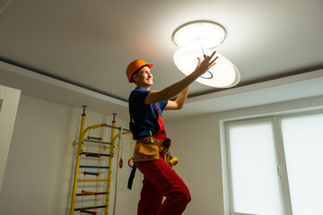 Worker installing lamp on stretch ceiling indoors. Space for text