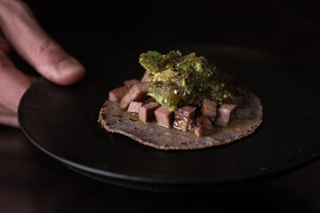 hand holding a dish with a cow tongue taco
