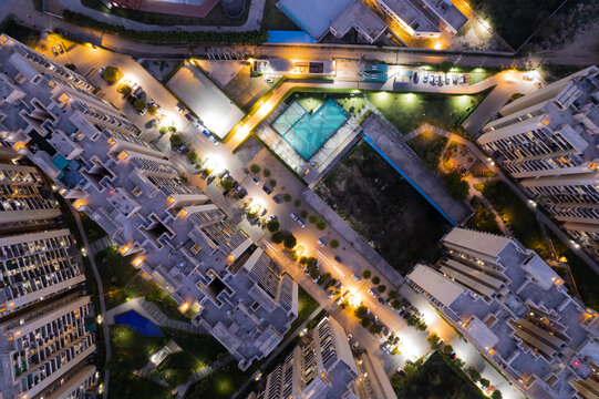 aerial drone shot ooking down over skyscrapers of a premium apartment complex with parking swimming pools with lights switched on at dusk twilight in gurgaon haryana India