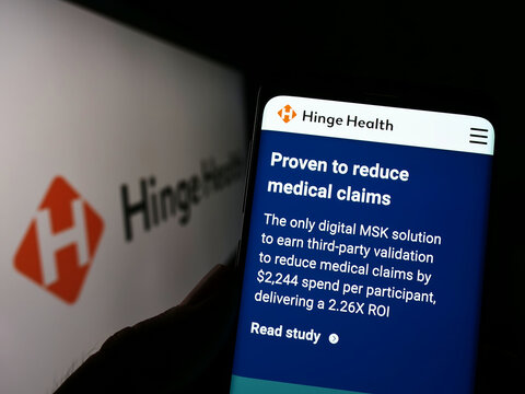 Stuttgart, Germany - 07-31-2022: Person holding cellphone with webpage of US digital clinic company Hinge Health Inc. on screen in front of logo. Focus on center of phone display.