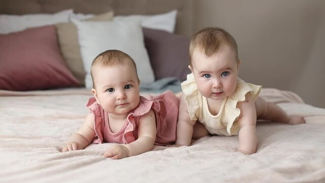 Portrait of two cute little baby girls twins lying side by side in a soft cozy bed at home