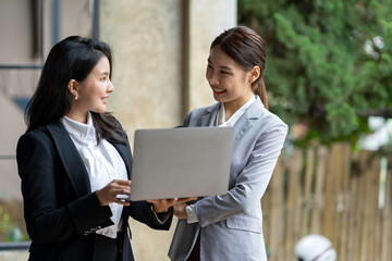 Two pretty young Asian businesswomen standing to discuss working on investment projects and...