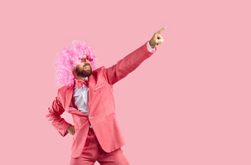 Smiling man in funny wig isolated on pink studio background point up at empty copy space. Happy...