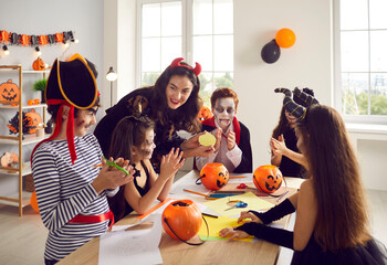 Playful teacher learn together with children celebrate Halloween in school. Smiling tutor study...