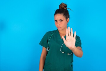 beautiful doctor woman wearing medical uniform over blue background shows stop sign prohibition...