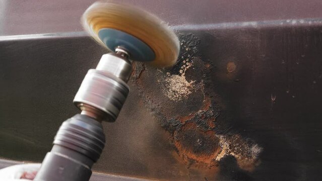 A round metal brush in the hands of the master cleans rust and paint from the car door. Medium plan