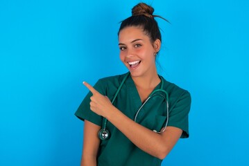 beautiful doctor woman wearing medical uniform over blue background glad cheery demonstrating copy...