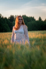 Fototapeta na wymiar Portrait of a young beautiful red-haired girl in glasses on a summer field in the evening. There is artistic noise.