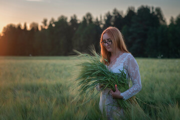 Portrait of a young beautiful red-haired girl in glasses on a summer field in the evening. There is artistic noise.