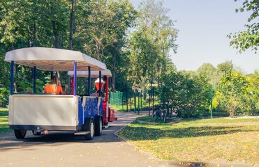 children and adults ride the train attraction in the park on a sunny summer or autumn day.