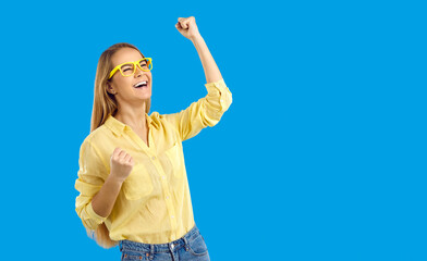 Overjoyed millennial Caucasian girl in glasses isolated on blue studio background scream celebrate...