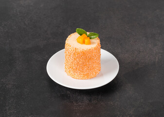 Apricot mousse cream chocolate dessert of cylindrical shape, sprinkled with colored coconut flakes, on a plate. Dark background