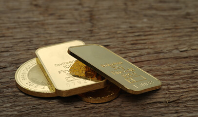 Gold bullion. Minted bars and coins on a wooden texture background. Selective focus.