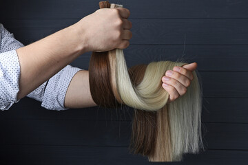 The male hand holds several sections of hair for extension.