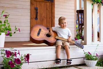 a little boy sits on the doorstep of his house and plays the guitar